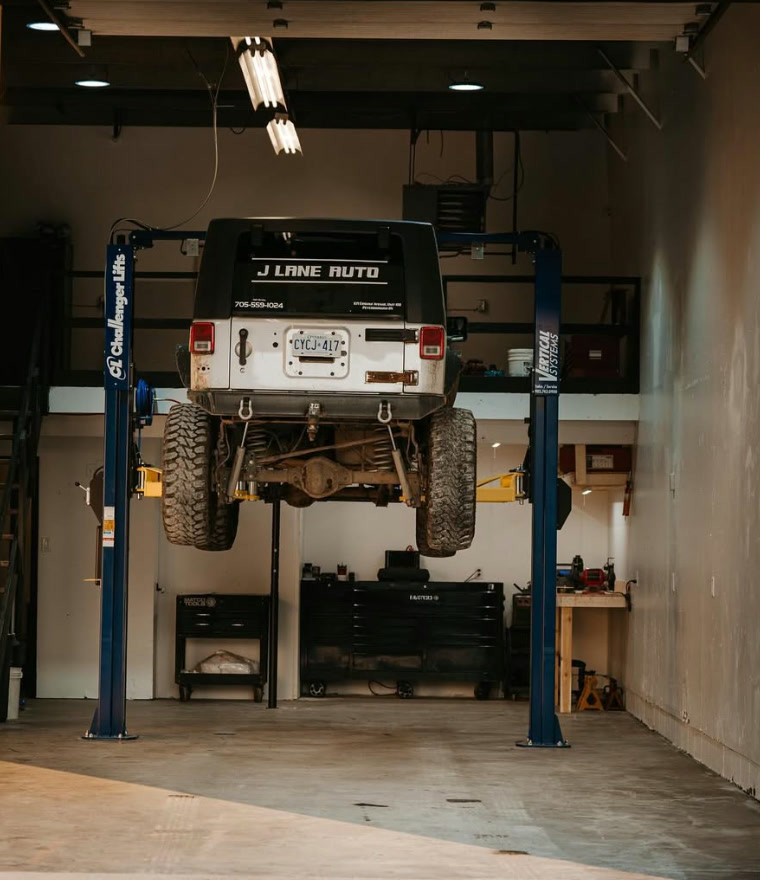 A lifted Jeep Wrangler on a two post hoist inside the J Lane Auto service bay