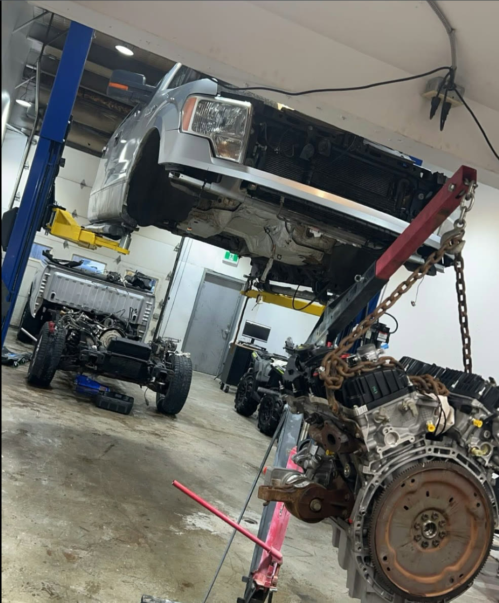 A Ford F-150 on the hoist with its engine out on a crane