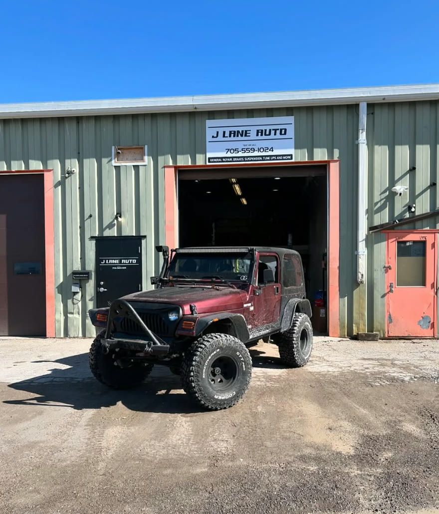 Maroon Jeep Wrangler TJ on mud tires outside the open bay